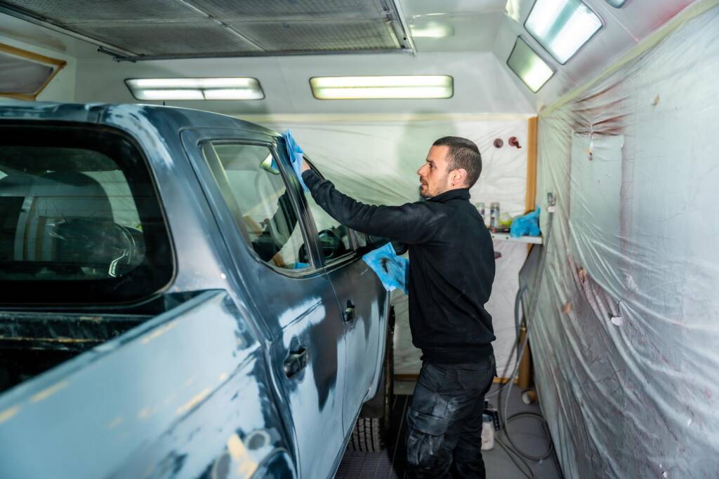 Van respray preparation process with technician sanding and cleaning vehicle panel inside a professional spray booth